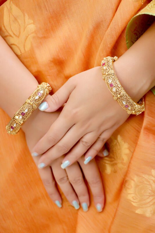 Key Features: Elegant filigree work with antique gold polish Ruby red square stones and tear-drop white embellishments Secure screw lock closure for easy wear Perfect for festive, bridal, and traditional wear Description: These Antique Ruby-Studded Gold-Plated Bangles reflect timeless Indian craftsmanship. With intricate latticework and ruby-red stone detailing, they bring royal elegance to your festive attire. Perfect to pair with sarees, lehengas, or ethnic suits, these bangles add a regal touch to every celebration.