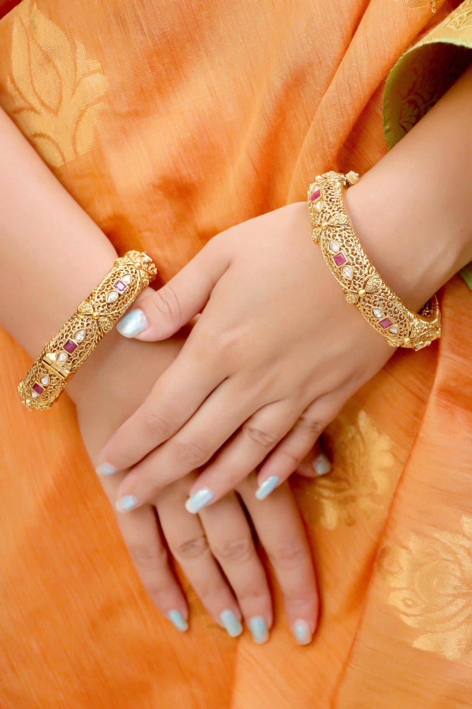 IMG_0761 Key Features: Elegant filigree work with antique gold polish Ruby red square stones and tear-drop white embellishments Secure screw lock closure for easy wear Perfect for festive, bridal, and traditional wear Description: These Antique Ruby-Studded Gold-Plated Bangles reflect timeless Indian craftsmanship. With intricate latticework and ruby-red stone detailing, they bring royal elegance to your festive attire. Perfect to pair with sarees, lehengas, or ethnic suits, these bangles add a regal touch to every celebration.